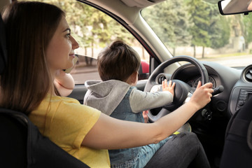 Mother with little son on knees driving car and talking by phone. Child in danger