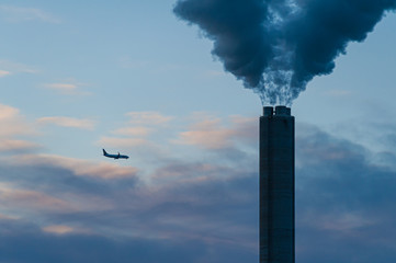 Airplane passing behind large chimney with smoke