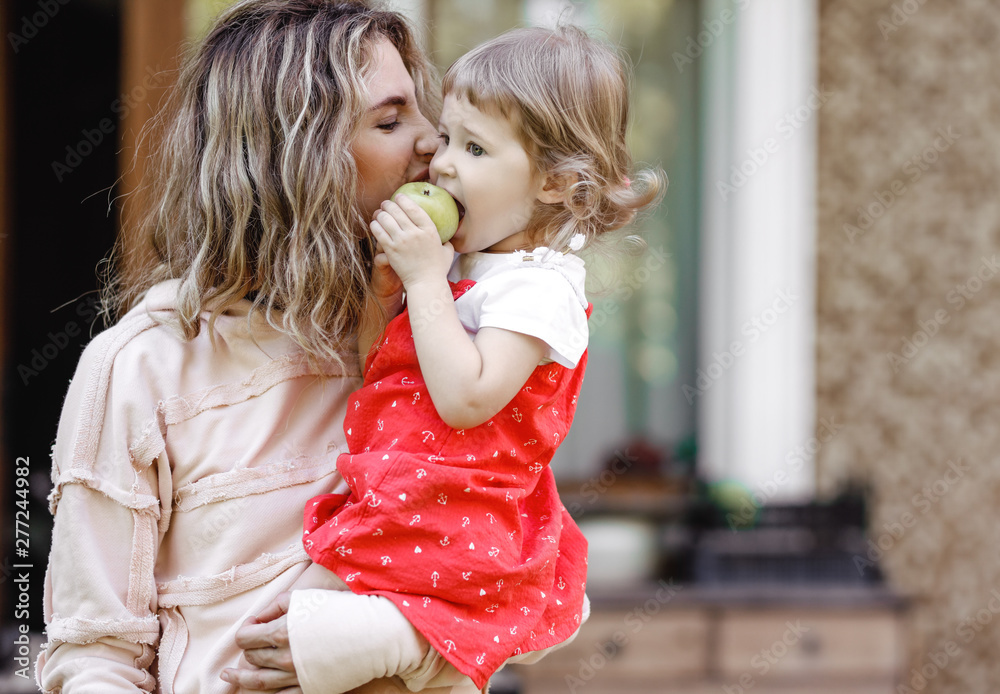 Young mother holds her little daughter on her hands and kisses her ...