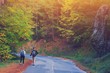 © raisondtre - Rear view of young couple walking on road through woods with backpacks. Man and woman hiking in forest. Active adventure, travel, tourism, hike and people lifestyle concept. Beautiful forest nature.