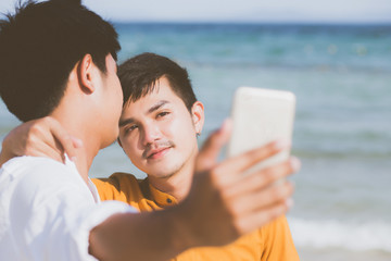 Gay portrait young couple smiling taking a selfie photo together with smart mobile phone at beach, LGBT homosexual lover in the vacation at sea, two man going to travel, holiday concept.