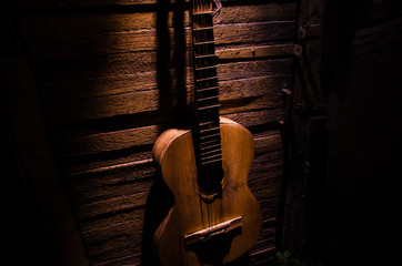 Wall Mural - An wooden acoustic guitar is against a grunge textured wall. The room is dark with a spotlight for your copyspace.