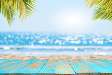 Wall Mural - Top of wood table with seascape and palm leaves, blur bokeh light of calm sea and sky at tropical beach background. Empty ready for your product display montage.  summer vacation background concept.