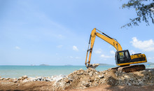 Excavator Digger Stone Working On Construction Site - Backhoe Loader On The Beach Sea Ocean And Blue Sky Background