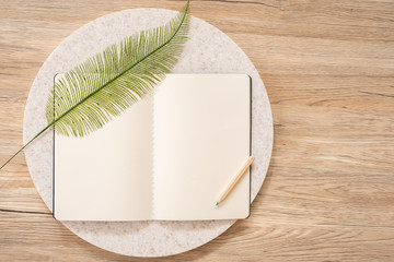 Poster - top view of open notebook with leaf and pencil on wooden table with copy space.eco sustainable concept.