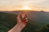 Fototapeta Koty - Female hand with compass in summer mountains at sunrise, pov.