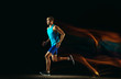 © master1305 - Professional male runner training isolated on black studio background in mixed light. Man in sportsuit practicing in run or jogging. Healthy lifestyle, sport, workout, motion and action concept.