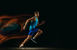© master1305 - Professional male runner training isolated on black studio background in mixed light. Man in sportsuit practicing in run or jogging. Healthy lifestyle, sport, workout, motion and action concept.