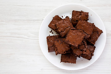 Top view, homemade chocolate brownies on a white plate on a white wooden background. Flat lay, overhead, from above. Copy space.