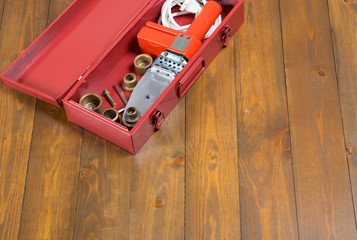 on a dark wooden background, a red box with a soldering iron and a set of nozzles for the repair and construction of plastic pipes, with a place for the inscription