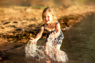 little girl by the river in summer splashes water