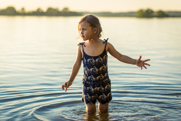  little girl by the river in summer splashes water