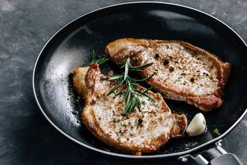 Poster - Roasted pork steaks in a frying pan with rosemary and garlic close up.