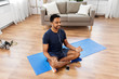 © Syda Productions - fitness, meditation and healthy lifestyle concept - indian man in earphones listening to music on smartphone and meditating in lotus pose at home