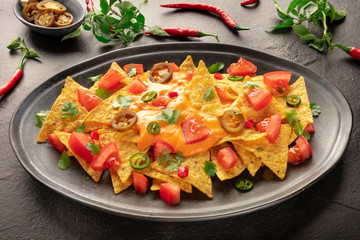 Mexican nachos with a cheese sauce, chili and jalapeno peppers, tomatoes, and cilantro on a black background