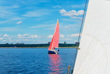 Sailboat With Red Sails On The Background Of The Shore With An Urban Landscape