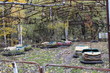 Old broken rusty metal radioactive yellow cars, children's electric cars, abandoned among vegetation, the park of culture and recreation in the city of Pripyat, the Chernobyl disaster, Ukraine.