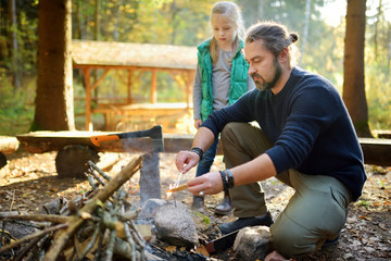 Wall Mural - cute young girl learning to start a bonfire. father teaching her daughter to make a fire. child havi