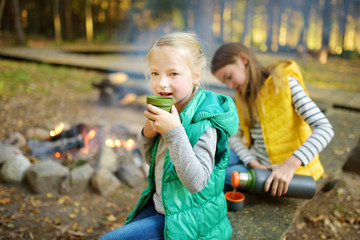 Wall Mural - cute young girl drinking tea and roasting marshmallows on stick at bonfire. child having fun at camp