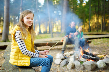 Wall Mural - cute little sisters and their father roasting marshmallows on sticks at bonfire. children having fun