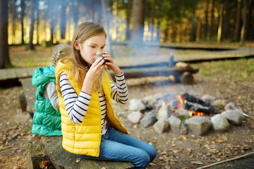 Wall Mural - cute young girl drinking tea and roasting marshmallows on stick at bonfire. child having fun at camp
