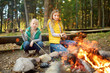 © MNStudio - Cute young sisters roasting hotdogs on sticks at bonfire. Children having fun at camp fire. Camping with kids in fall forest.