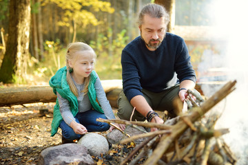 Wall Mural - cute young girl learning to start a bonfire. father teaching her daughter to make a fire. child havi