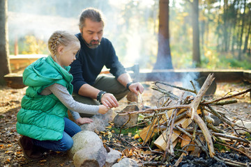Wall Mural - cute young girl learning to start a bonfire. father teaching her daughter to make a fire. child havi