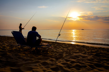 silhouette of two friends who are fishing on the beach in sunrise morning