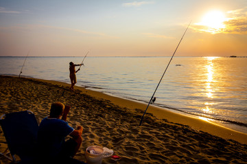 Silhouette of two friends who are fishing on the beach in sunrise morning