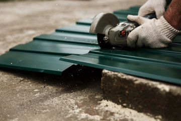 The master cuts a professional metal sheet for installation on the roof of the house. Roofer cutting metal roof sheets, metal tile for house roofing construction.