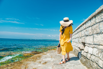 Wall Mural - woman in yellow sundress at sea beach in straw hat