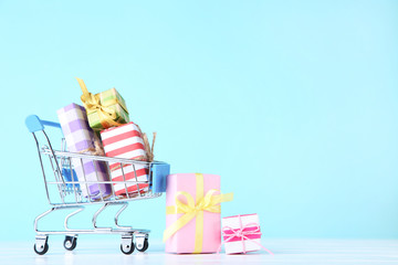 Wall Mural - Small shopping cart with gift boxes on blue background