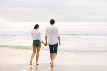 A Man And Woman Hold Hands And Walk Along The Sand Or Along The Beach By The Sea.