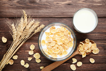 Corn flakes in milk with wheat ears on brown wooden table