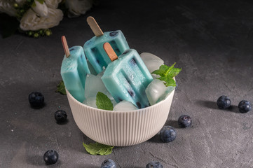 Blue popsicles with blueberries on dark background