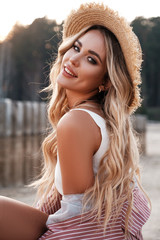 Wall Mural - Close portrait of a pretty, romantic and cheerful country girl with long loose hair in a straw hat. Sunlight, soft sunny colors. Nature landscape. Countryside at the background. Summer, summertime