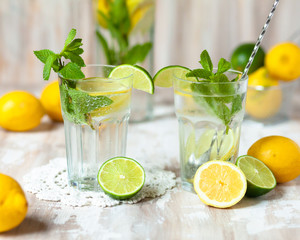 Summer composition with refreshing healthy alcohol free home made lemonade with pepper mint, limes and lemons. White lace napkin as decor, wooden background. Vacation mood, enjoying summertime