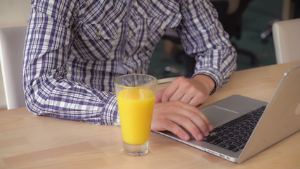 Aufkleber - Male hands typing on keyboard laptop. On the wooden table glass with orange juice. Close up details.