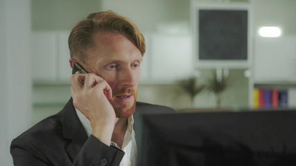 Poster - Red-haired man sitting at a computer and calling on the phone. UHD