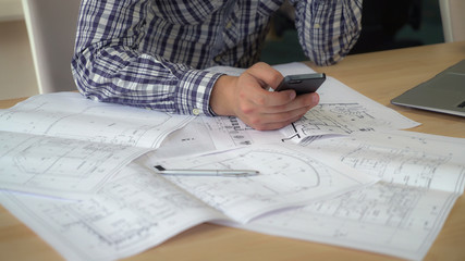 Aufkleber - Designer using mobile phone works with plan building. take photo of sketch and send client or sharing in social net. Man hands holding smartphone texting message at the working place. On the wooden