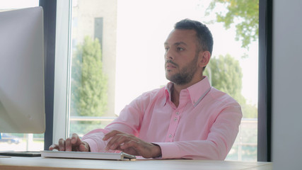 Poster - Portrait mixed race man working at home office. Adult man typing on keyboard looking on monitor computer. Guy sitting in room with big windows