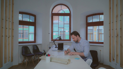 Aufkleber - adult professional architect working with blueprint holding pencil and straightedge. Handsome caucasian man wearing in casual dress sitting in the office.