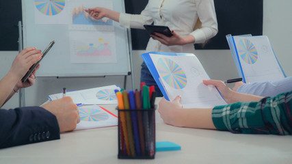 Poster - Closeup business team sitting around desk in boardroom. People holding paper report with financial data. Women and men make notes in documents with different colored graphs and diagrams. Speaker