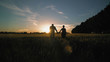 © vadosloginov - Family walks at sundown rear back view. People with dog nature view at sunset. Silhouettes man and woman walking on the field holding hands running little french bulldog. breathtaking scenery in