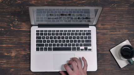 Fototapete - top view male hand scrolling on computer. Working place with wooden desk cup with coffee and laptop.