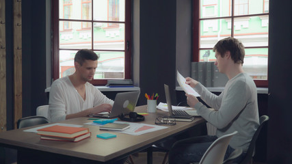 Aufkleber - Young professional start up team working in modern office. Caucasian men computing on laptop and discussing project. Handsome man wearing in casual clothes talking with friend at work. Smiling workers