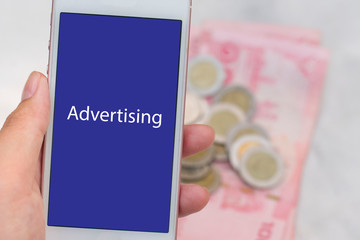 Social media advertising. Smartphone show text Advertising on screen and Thai money in the background.