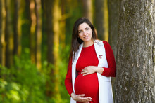 Pregnant In Red. Portrait Of A Beautiful Pregnant Woman In A Red Dress In The Flowering Spring Park