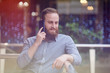 © ruslanshug - happy smiling young cute caucasian male with beard calling with cell telephone indoors